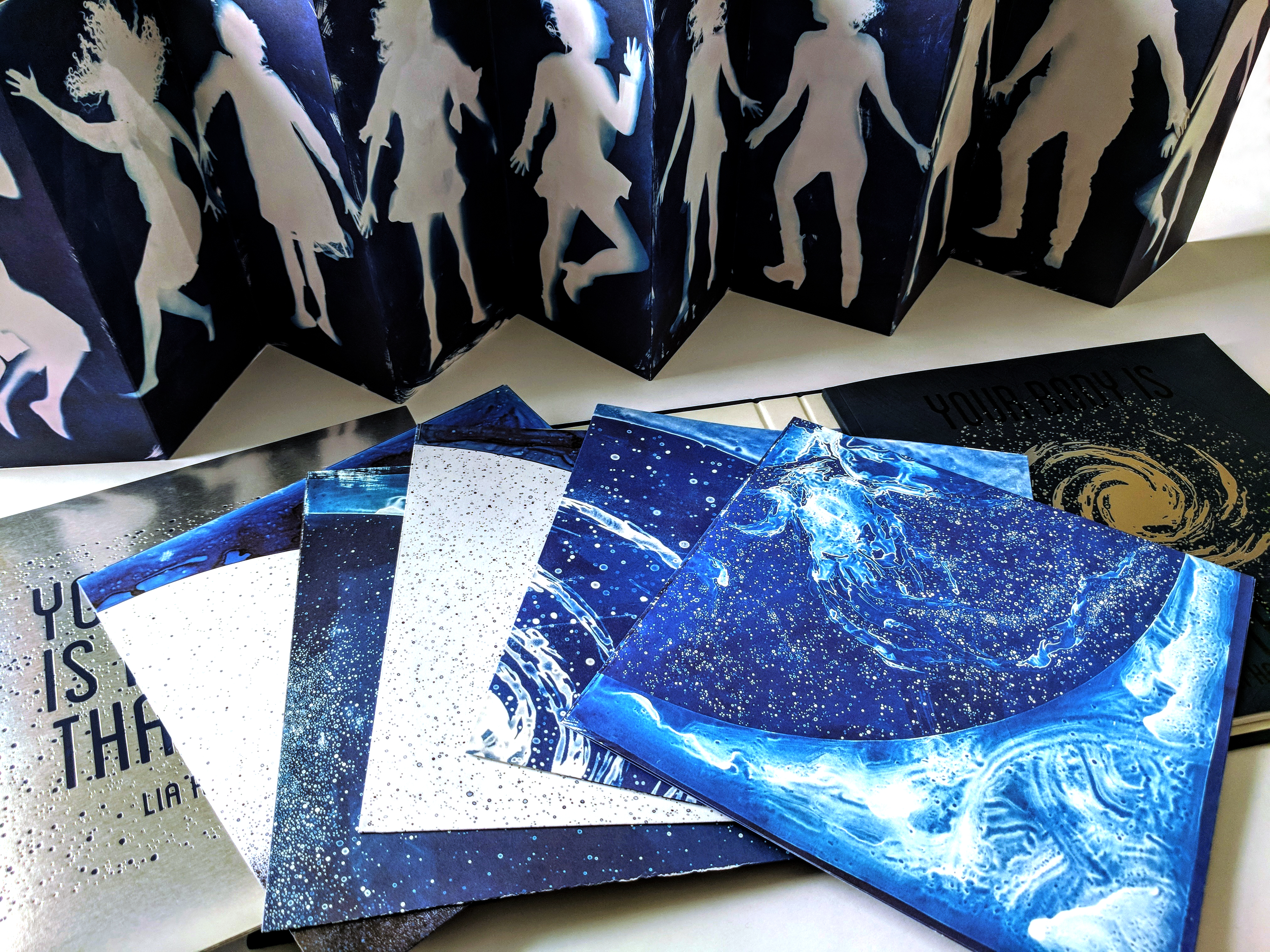 Five individual square 9x9 posters included in the mylar envelope, folded and fanned out on top of open art book.