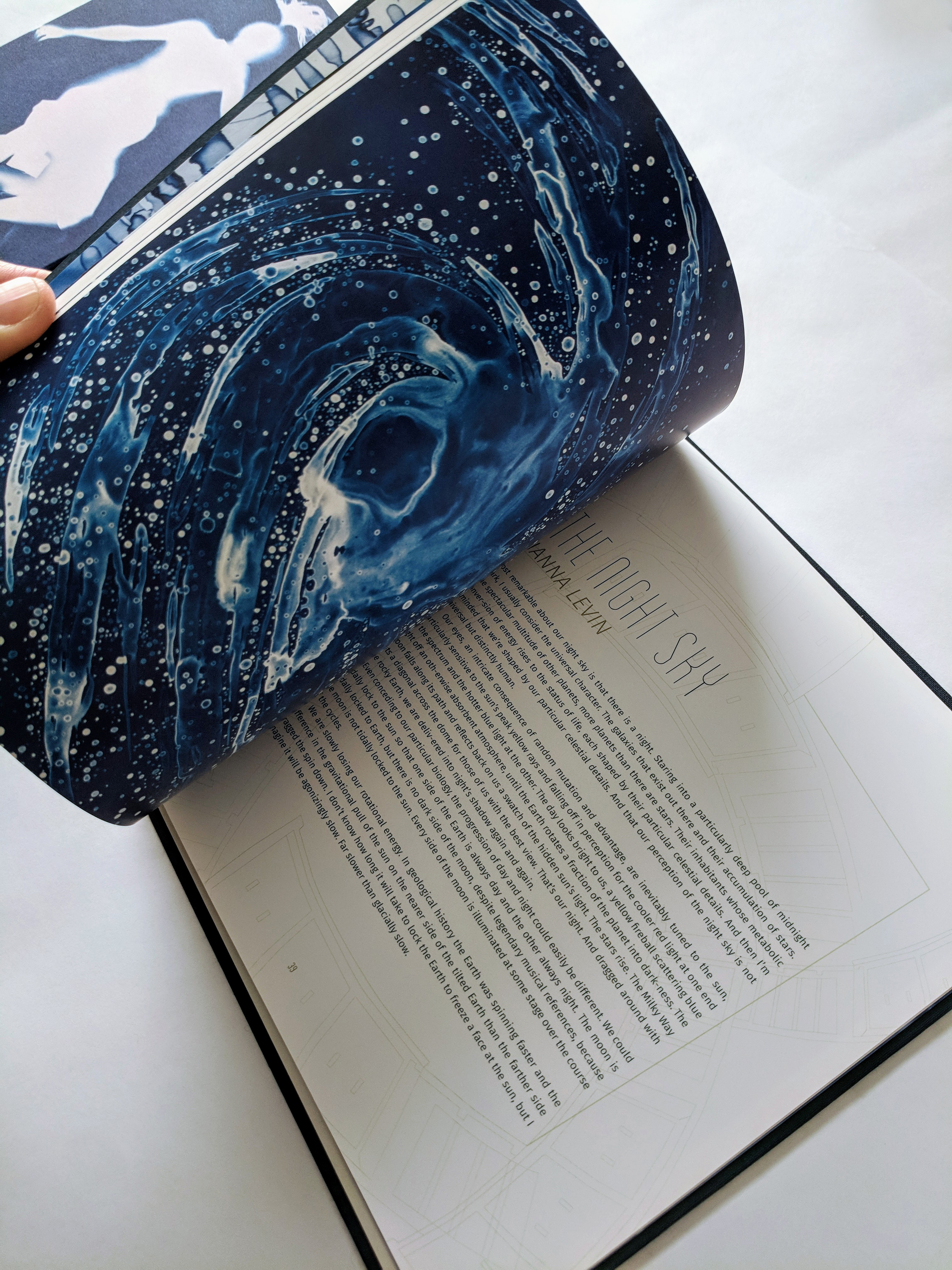 Hand opening softcover book showing essay by Janna Levin and Lia's drawing on the opposing page